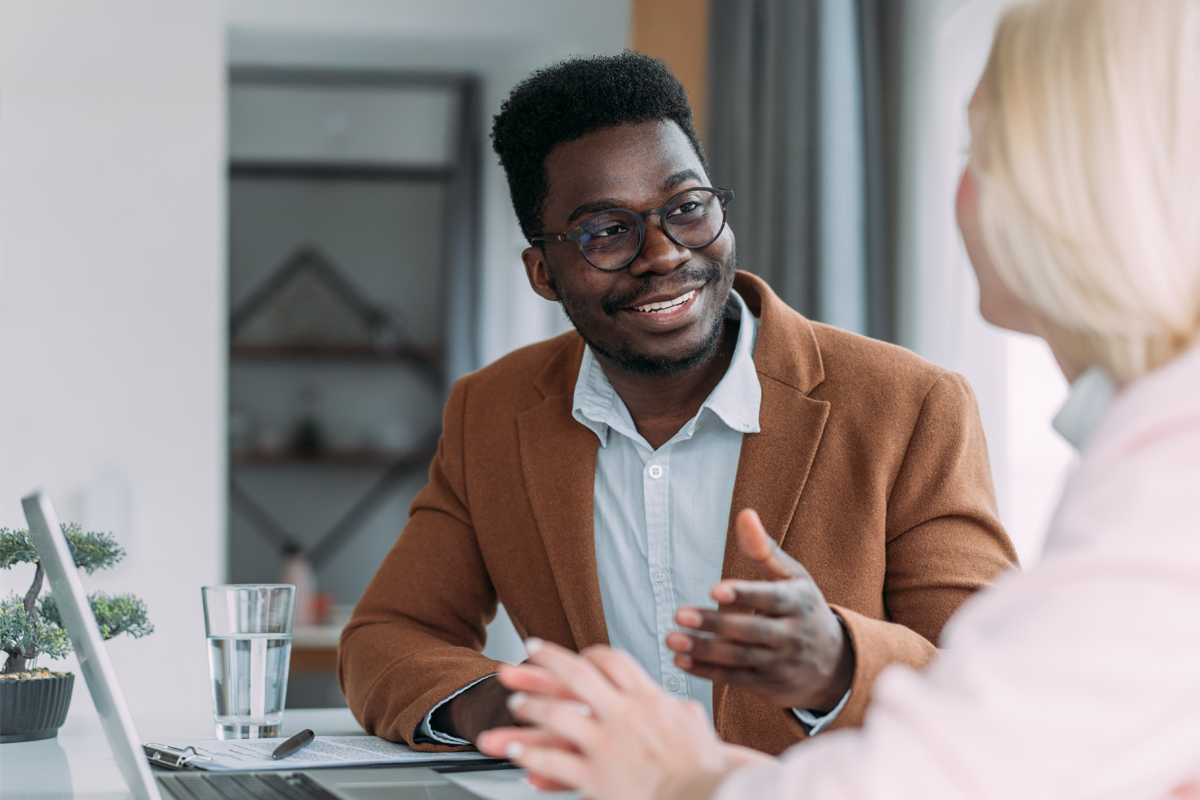 man sitting at table with laptop speaking to woman