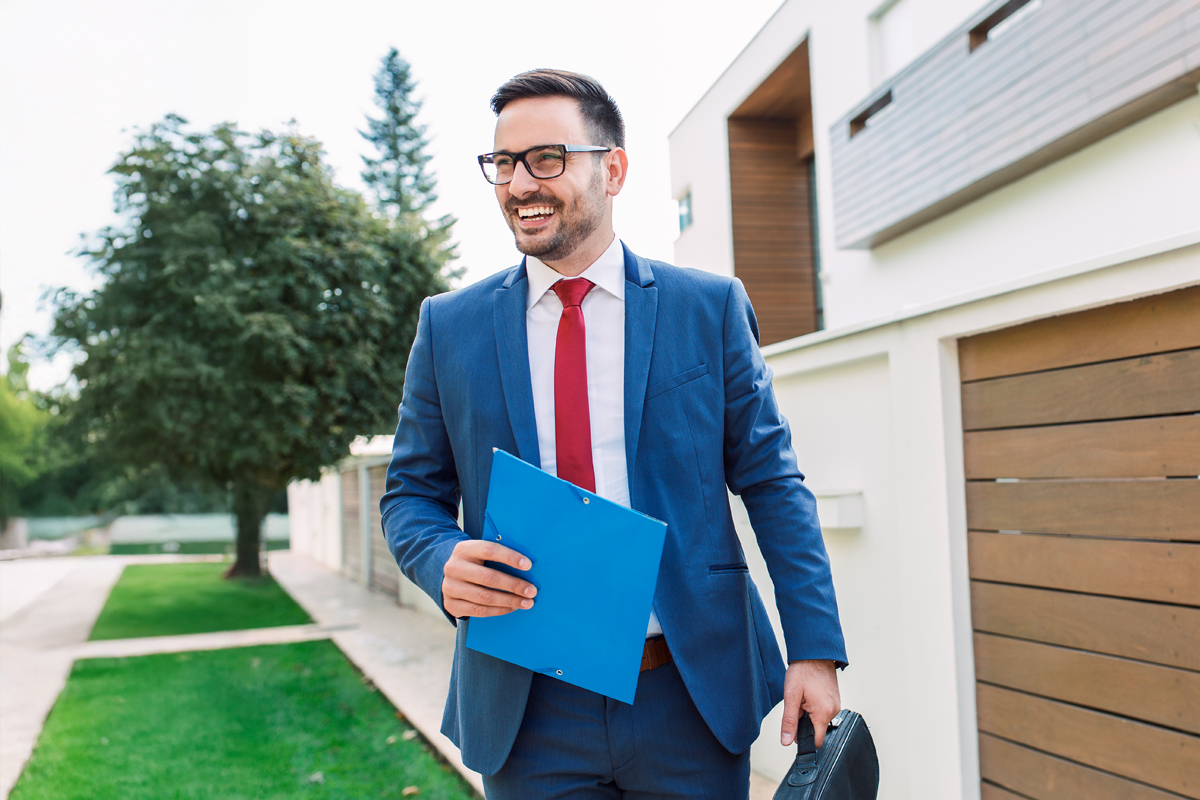 man walking outside of a residential home in suite holding files